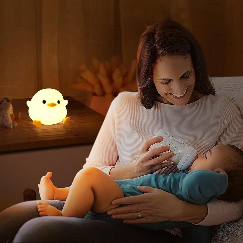 Woman holding a baby and feeding them with a bottle, with a glowing night light in the background.