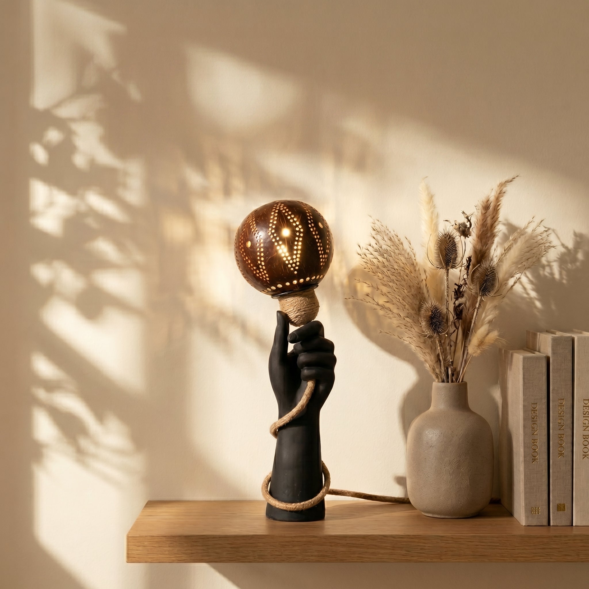 Decorative lamp with a hand holding a bulb on a wooden shelf with books and a vase.